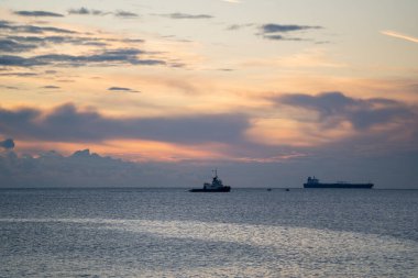 Gün doğumunda Sakin Deniz 'de iki kargo gemisi, Yumuşak Pastel Bulutları ve Geniş Horizon Yazı Uzağı Siluetleri, Yumuşak Dalgalar ve Serin Şafak Paleti Oluştur