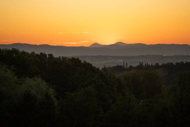 Yumuşak alacakaranlık sisi vadide katmanlı tepeler ve sakin pastel gökyüzü ile dalgın bir ruh hali uyandırıyor.