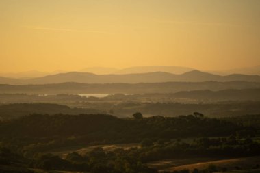 Yuvarlanan vadilerin üzerinde sisli gün doğumu, katmanlı tepeler arasında süzülen yumuşak sis ve ısınan güneş çizgileri.