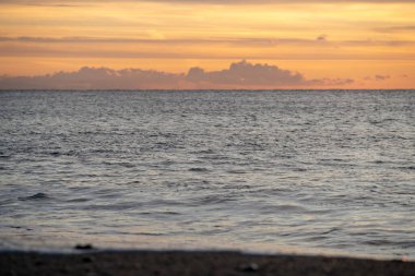 Sakin Deniz 'in üzerinde gün doğumu ve çakıllı sahil, yumuşak altın ışık, uzun yansımaları geniş, boş, markalaşma ve arka plan kullanımı için ideal.