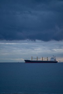 Şafak Fırtınalı Gökyüzünde Kargo Gemisi. Yalnız Yük Gemisi, Sakin Mavi Okyanus 'un Üzerinde Güneş Doğmadan Önce Oturuyor, Derin Bulutlar Üstümüzde Bulutlanıyor, Moody Silueti, Metin İçin Geniş Negatif Alan,