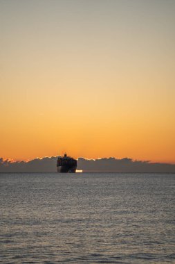 Gündoğumundan önce sakin denizde kargo gemisi, geniş ufuk ve boş gökyüzü pazarlama ve editoryal kullanım için sessiz altın tonlar ve metin ve markalaştırma için yer sunar.