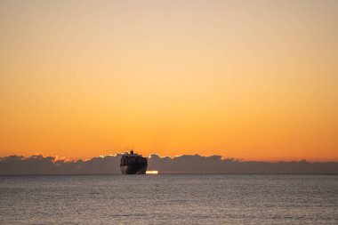 Şafakta gemi, güneş doğarken geniş bir alana yayılmış, geniş turuncu gökyüzü altında gün ışığının tadını çıkaran, geniş bir kargo gemisi.
