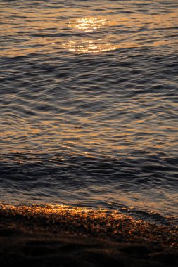 Sakin sahilde gün doğumunda altın dalgalar, yumuşak parıltılı seçici odak ve yansıtıcı dalga desenleri, sıcak kehribar gölgeleri, meditasyon havası, uzayla dikey kompozisyon