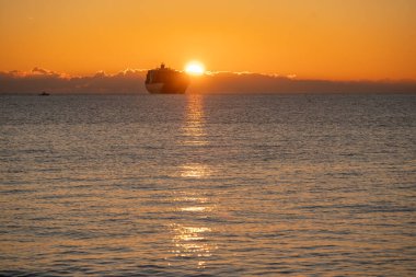 Geniş günbatımı gökyüzünün altında geniş turuncu gökyüzü, geniş bir kargo gemisi sosyal medya başlıkları ve afişleri için ideal geniş turuncu ufuk çizgisine kurulmuş.