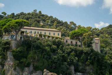Issız uçurum tepesindeki villa yemyeşil çam ağaçlarının arasında, parıldayan denize bakan dramatik kayalıklara tünemiş taş cephe