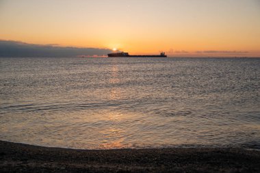 Sabah ışığı sahnesi, huzurlu okyanusun üzerinde parlak bir gün doğumu uzak bir tekne parıldıyor, sabahın erken saatlerinde güneş sakin sahili boyuyor ve parlak yansımalarla sakin suları boyuyor.
