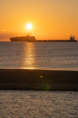 Sabahın erken saatlerinde, uzak gemi ve sükunetle ışıldayan okyanus, yükselen güneşe karşı geminin silueti gibi okyanusun üzerinde huzurlu bir şekilde parıldıyor.