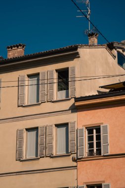 Pastel cephelerde kepenkler ve çatı çizgileri, antenler ve bacalar derin mavi gökyüzüne karşı siluet, gün ortası ışığı Akdeniz dokusunu, sakin mahalle manzarasını gözler önüne serer,