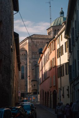 Altın ışıklı bazilika ve dar sokaklar, taş duvarlar ve park etmiş scooterlar, yayalar gezinen, karmaşık duvarlar ve kubbe ayrıntıları, samimi şehir ölçeği, geç kalmalar.
