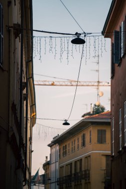 Antika lambalar tarihi şehir sokaklarını aydınlatır, alacakaranlık pastel binaları sıcacık parlaklıkta, kaldırım taşlı yollarda ve sicim ışıkları Parma 'da neşeli bir günbatımı atmosferi yaratır.