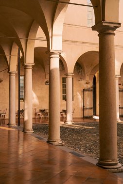 Parma şehrinde arcaded manastır terracotta zemin ve yumuşak altın ışık, uzun sütunlar ve yuvarlak kemerler cilalanmış fayanslar, ıslak kaldırımlar ve yıpranmış