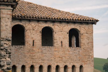 Parma kırsalında tuğla palazzo cephesi terracotta çatı kiremitleri, kemerli pencereler yıpranmış duvarlar ve yuvarlanan tepelere bakan küçük açıklıklar, sessiz kırsal siluet