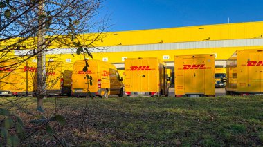 Alman posta servisinin sarı elektrik dağıtım araçları Almanya 'nın Waiblingen (Stuttgart tarafından) lojistik merkezinde 26.12.2025' te şarj ediliyor. Paket taşıma işlemlerinin dikey görünümü, modern lojistikte elektrikli araçların kullanımı