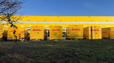 Alman posta servisinin sarı elektrik dağıtım araçları Almanya 'nın Waiblingen (Stuttgart tarafından) lojistik merkezinde 26.12.2025' te şarj ediliyor. Paket taşıma işlemlerinin dikey görünümü, modern lojistikte elektrikli araçların kullanımı