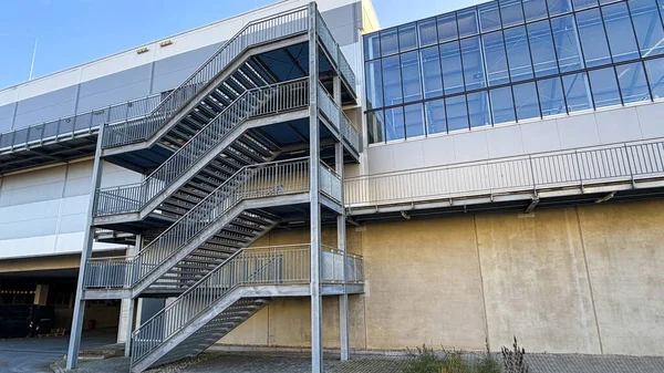 Dış cepheye bağlı metal bir merdiven bulunan sanayi deposu. Yapı beton duvarlar ve büyük cam yüzeyler, modern endüstriyel mimari, teknik altyapı ve lojistikle ilgili tesisleri birleştiriyor.