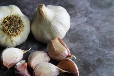 Sarımsak soğanları ve soyulmuş karanfiller koyu gri bir mutfak arka planında oturuyorlar.