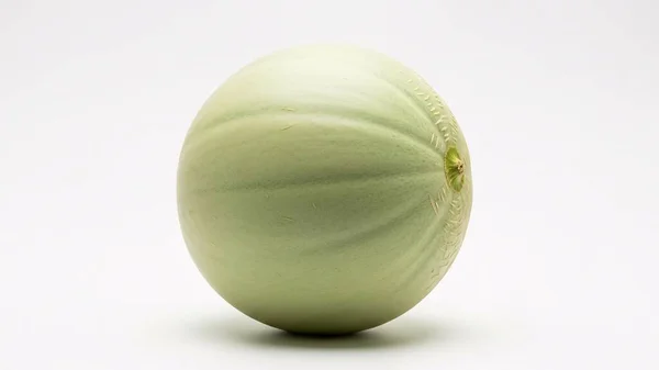 Olgun bir kavun, pürüzsüz, soluk yeşil derisini ve ince sırtlarını sergileyerek beyaz bir zemine yaslanır. Sağlıklı ve ferahlatıcı bir meyve.