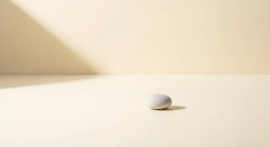 Yalnız, pürüzsüz bir çakıl taşı, yumuşak gölgeli, parlak beyaz bir masanın üstünde durmaktadır..