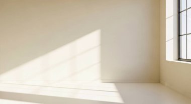 Bright empty room bathed in warm sunlight creating clean geometric shadows on a pale wall