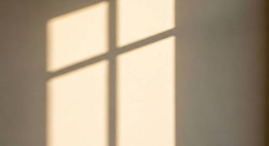 Ilık güneş ışığı pencereden içeri akar ve duvarda yumuşak dikdörtgen bir ışık demeti oluşturur..