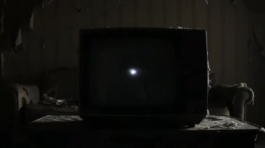 Eski bir televizyon, loş ve çürüyen bir odada statik bir görüntü sergiliyor. Video, statik ekranı ve çevreyi gösteriyor..