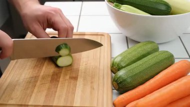 Ahşap kesme tahtasındaki havuç ve kabağı dilimlemek için bıçak kullanan ellerin yakın çekimi. Sebzeler yemek için hazır..