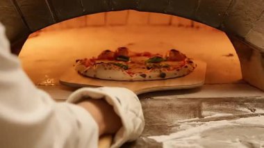 Tahta fırından bir pizza çıkarılıyor. Pizza ahşap bir kabuğun üzerinde..