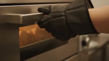 Eldivenli bir el, içinde pişen bir tepsi altın rengi kruvasanı ortaya çıkarmak için fırını açar ve pişirme sürecini gösterir..