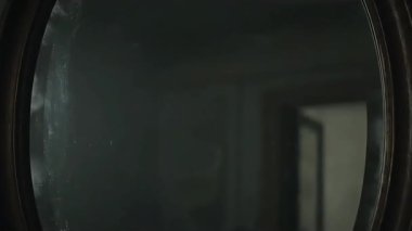 Karanlık, antika bir ayna gölgeli bir figürü yavaşça ortaya çıkarıyor. Belirsiz atmosfer.