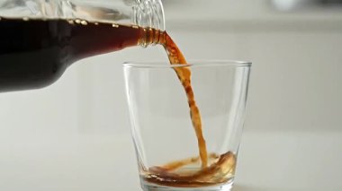 Yakından, şişeden dökülen koyu bir sıvının temiz bir bardağa döküldüğü bir video..