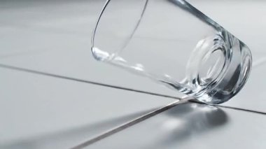 Bir cam takla atıyor ve ağır çekimde beyaz bir zeminde kırılıyor..