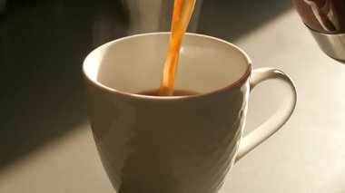 Sıcak kahvenin beyaz bir fincana, buharlı, güneş ışığına döküldüğü videoyu kapat.