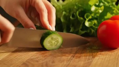 Bir insan salatalık dilimleyerek, domates ekleyerek ve ahşap kesim tahtasına marul yaprağı koyarak taze bir salata hazırlar..