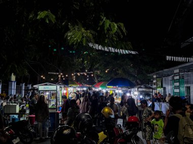 Hareketli bir gece marketinin enerjisini hissedin. İnsanların festival ışıkları altında sokak yemeklerinin ve topluluğun keyfini çıkardığı canlı bir sahne. Kültürle dolu bereketli ağaçlar..