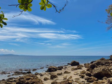 Huzurlu bir tropikal cennete kaçmak. Kristal mavi sular engebeli, güneşli bir kıyı şeridiyle buluşur. Uçsuz bucaksız, bulutlu bir gökyüzünün altında. Seyahat, doğa ve kaçış temaları için mükemmel..