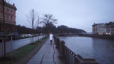 Beyaz ceketli bir kız caddede yürüyor. Moika nehrinin kıyısında genç bir kadın. Bulutlu Saint Petersburg.