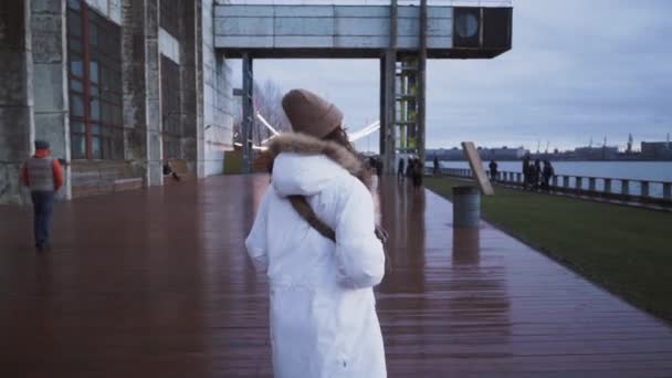 Chica noruega camina por la calle. Paisaje marino borroso escandinavo. Una joven con una chaqueta blanca. Nublado paisaje dramático nublado. Hora azul — Vídeos de Stock