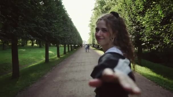 Йди за мною. Молода біла дівчина пропонує слідувати за нею з рукою до парку. Повільний рух — стокове відео