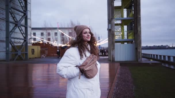 Norska tjejen går nerför gatan. Skandinaviska Foggy sjölandskap. Ung kvinna i vit jacka. Molnigt mulet dramatiskt landskap. Blå tid — Stockvideo