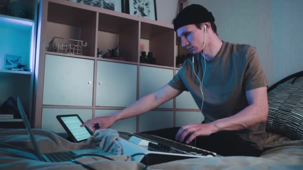 Young caucasian guy sitting in his bedroom and playing on MIDI keyboard or synthesiser and making electronic music.Dj slow motion footage — Stock Video