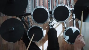 Evde elektronik davul çalan bateristin üst görüntüsü. Dairede sopalı perküsyon dersleri. Rock müzik performansı. 60 fps yavaş çekimde olabilir.