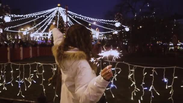 Menina encaracolado com sparkler. Jovem alegre com luzes cintilantes de Ano Novo. Personagem sorridente em uma jaqueta branca. Conceito de Natal e Inverno. — Vídeo de Stock