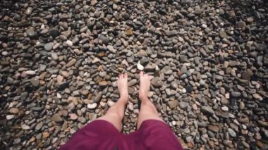 Çakıl taşı plajında ayaklar. Bir adam taşların üzerinde yalınayak yürüyor. Köpüklü dalgalar. Fransa 'da Gök Denizi.