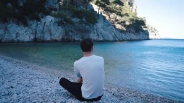 Adam doğayı, dağları ve masmavi denizi seviyor. Genç bir adam Fransa 'nın güneyindeki kayaları keşfediyor. Kot pantolon ve eski tarz modaya uygun bir karakter. Cassis 'teki tropikal manzara.