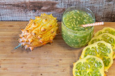 Boynuzlu kavun, kiwano olarak da bilinir, dilimlenmiş ve ahşap kesme tahtasındaki ferahlatıcı yeşil bir meyve suyuyla harmanlanmış.