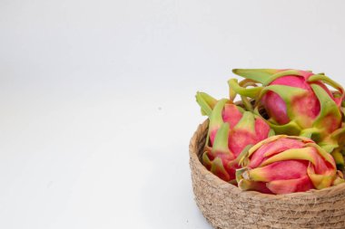 Pitaya olarak da bilinen ejderha meyvesi, canlı pembe deri ve yeşil pullar sergiliyor, doğal dokuma sepetinde oturuyor.