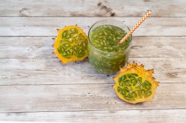 Boynuzlu kavun (kiwano) yeşil köhne hamuru ortaya çıkarmak için ikiye bölündü. Ahşap bir masanın üzerinde yenilenen bir bardak meyve suyu, stüdyo masrafları.