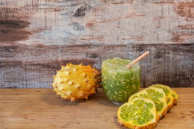 Kiwano kavunu, bütün ve dilimlenmiş, canlandırıcı bir meyve suyu ile, ahşap bir arka planda. Sağlıklı yaşam için egzotik meyve