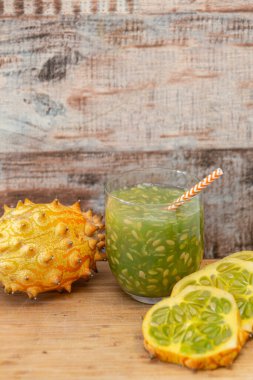 Boynuzlu kavun, aynı zamanda kiwano olarak da bilinir, tohumlarla ferahlatıcı bir meyve suyu yaratır, bütün olarak sunulur ve ahşap arka planda dilimlenir.